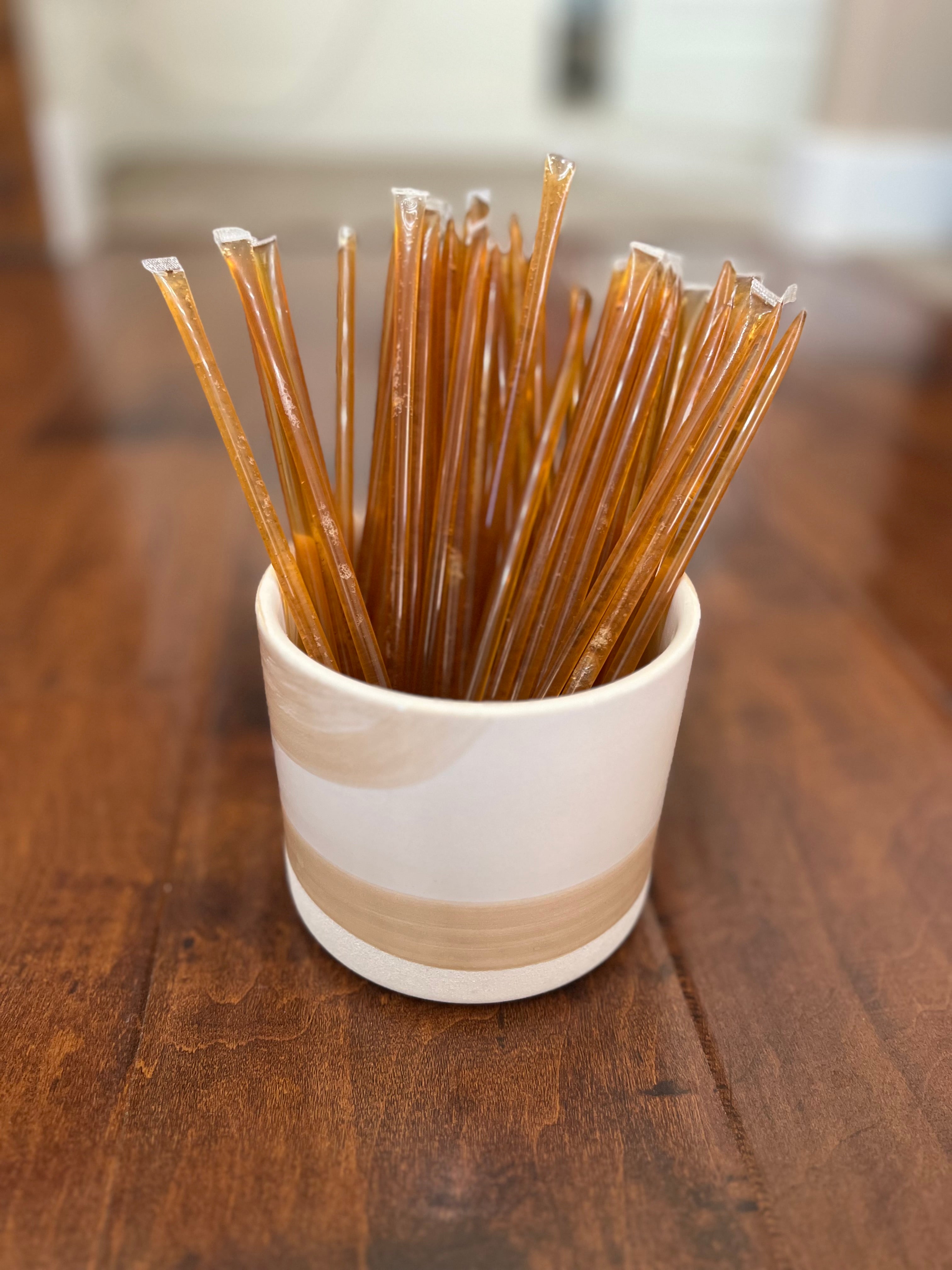 Raw Unfiltered Local honey straws for snacking in a white cup on a wood table in St. George Utah.